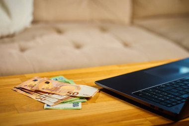 Tahta masadaki Avrupa banknotları ve dizüstü bilgisayarlar. Nakit ödemeler, tasarruflar ve kişisel finans kavramı
