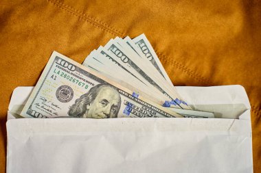 Beyaz zarfın içinde dolar banknotları, üst manzara. Kahverengi arka plandaki nakit parayı kapat. Yolsuzluk, rüşvet ve gizli nakit ödeme kavramı