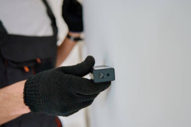 Eldivenli inşaat işçisi duvarı incelemek için lazer mesafe ölçer kullanıyor. İnşaatçı tamir sırasında hassas ölçüm için dijital araç kullanır. İnşaat ve yenileme konsepti