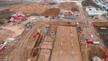 İnşaat alanının vinçlerle, vakıflarla ve inşaat malzemeleriyle hava görüntüsü. İkamet binası yapım aşamasında. Küçük kasabada yeni gelişmeler