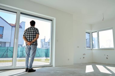 Yeni boş bir dairede dikiz aynasından modern yerleşim yerlerinin penceresinden dışarı bakan bir adam. Gayrimenkul yatırımı, emlak alımı ve konut yenileme kavramı