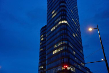Gece gökyüzüne karşı aydınlatılmış ofis pencereleri olan modern cam gökdelen. Gece manzarasında parlayan ışıkları olan yüksek katlı ofis binası.