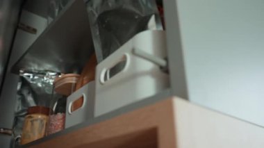 İnsan mutfak rafından yiyecek kabı ve cam bezle dolu kavanozu alır. Kadın mutfak dolabının kapısını açtı.