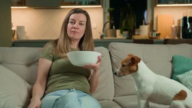 Kadın televizyon kumandası tutuyor ve köpek yanında otururken bowling oynuyor. Rahatlık, dostluk ve rahat ev hayatı kavramı