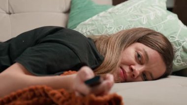 Kanepede uzanmış elinde uzaktan kumandayla televizyon seyreden bir kadın. Dinlenme, tembellik ve günlük yaşam tarzı kavramı