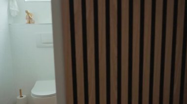 Minimalist tuvalet odası, duvara monte edilmiş klozet girişe bakıyor, taş lavabo ve ahşap zemin. Modern dairede çağdaş küçük banyo iç mimarisi