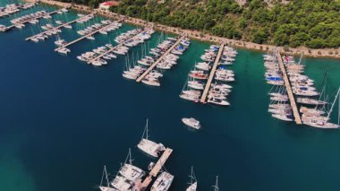 İskeleler boyunca rıhtımda liman manzaralı lüks yatlar. Liman, yeşil kıyı şeridinde yelkenli teknelerle dolu. Yaz seyahati, tatil ve deniz faaliyetleri kavramı