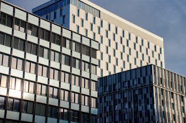 Şehirde cam ve beton cepheli modern ofis binaları. Modern şehir manzarasında yansıtıcı pencereleri ve geometrik cepheleri olan çağdaş gökdelenlerdeki kurumsal ofisler