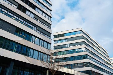 Şehirde cam ve beton cepheli modern ofis binaları. Modern şehir manzarasında yansıtıcı pencereleri ve geometrik cepheleri olan çağdaş gökdelenlerdeki kurumsal ofisler