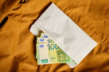 Avro banknotlarıyla dolu zarf, üst manzara. Kahverengi arka planda yakın plan para çekimi. Kişisel nakit tasarrufu ve zenginlik birikimi kavramı