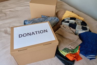 Evde bağış etiketli karton kutunun yanında kullanılmış giysiler. Sadaka, nezaket ve sosyal sorumluluk kavramı