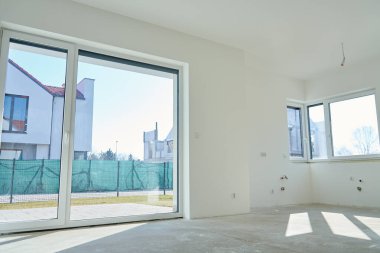 Geniş panoramik pencereli yeni bir daire. Panoramik cam kapıları ve yenilenmekte olan beyaz duvarları olan modern mobilyasız oda.