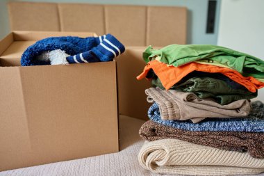 Yatakta bağışlanmış kıyafetlerle dolu açık bağış kutusu. Geri dönüşüm için kullanılmış giysilerle dolu bir karton kutu. Sadaka, nezaket ve sosyal sorumluluk kavramı