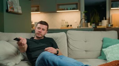 Adam elinde uzaktan kumandayla kanepede oturuyor. Kanepede dinlenen ve televizyon izleyen biri. Rahatlama, boş zaman ve ev eğlencesi kavramı