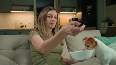 Kadın koltukta uzaktan kumandayla dinlenirken köpek yiyecek çalıyor. Ev sahibi televizyona odaklanırken evcil köpek kaseden yemek yiyor. Ev hayatı ve evcil hayvan davranış konsepti