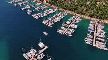 İskeleler boyunca rıhtımda liman manzaralı lüks yatlar. Liman, yeşil kıyı şeridinde yelkenli teknelerle dolu. Yaz seyahati, tatil ve deniz faaliyetleri kavramı