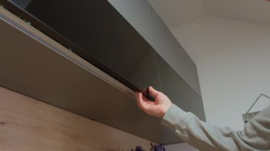 Adam üst mutfak dolabını açar ve içki bardağını alır. El, dolabı şeffaf bardaklarla açar.