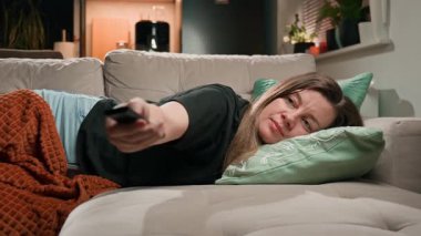 Kanepede uzanmış elinde uzaktan kumandayla televizyon seyreden bir kadın. Dinlenme, tembellik ve günlük yaşam tarzı kavramı