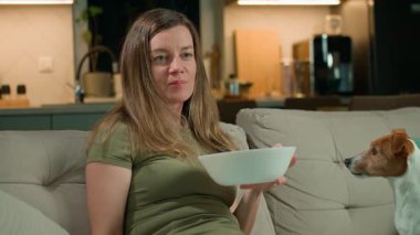 Kadın televizyon kumandası tutuyor ve köpek yanında otururken bowling oynuyor. Rahatlık, dostluk ve rahat ev hayatı kavramı