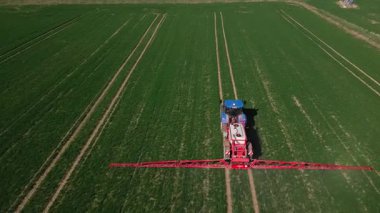 Tarım alanında çalışan mavi traktör, hava manzaralı. Traktör tarlasını gübrelemek veya iyi hasat için böcek ilacı ile ilaçlıyor. Çiftçilik teknolojisi ve mahsul bakımı kavramı