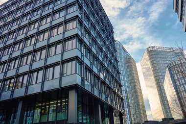 Şehirde cam ve beton cepheli modern ofis binaları. Modern şehir manzarasında yansıtıcı pencereleri ve geometrik cepheleri olan çağdaş gökdelenlerdeki kurumsal ofisler