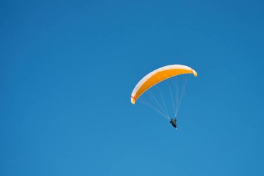 Mavi gökyüzüne karşı paraglider üzerinde uçuyor. Sarı gölgelikli paraglide. Olağanüstü spor