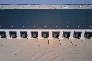 Lojistik deposunun dış tarafındaki yükleme platformlarının havadan görüntüsü. Dağıtım merkezinde kamyon ambarları ve kapalı yükleme kapıları. Nakliye işlemleri için ticari altyapı
