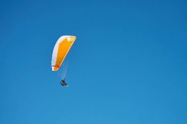 Mavi gökyüzüne karşı paraglider üzerinde uçuyor. Sarı gölgelikli paraglide. Olağanüstü spor