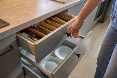 Kişi, ahşap çatal bıçak tepsisindeki çeşitli çatal bıçaklarla mutfak çekmecesini açar. Kadın mutfak dolabını açıyor. Ev organizasyonu ve işlevsellik kavramı