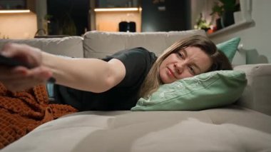 Kanepede uzanmış elinde uzaktan kumandayla televizyon seyreden bir kadın. Dinlenme, tembellik ve günlük yaşam tarzı kavramı