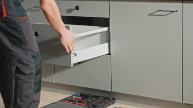 Adam modern dolapta tornavida kullanarak mutfak çekmecesini monte ediyor. Tamirci, çağdaş mutfağa çekmece kaydırma mekanizması kuruyor ve ayarlıyor. Mobilya kurulumu