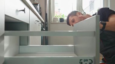 Adam modern dolapta tornavida kullanarak mutfak çekmecesini monte ediyor. Tamirci, çağdaş mutfağa çekmece kaydırma mekanizması kuruyor ve ayarlıyor. Mobilya kurulumu