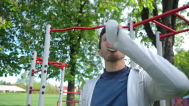 Atletik adam spor salonundaki spor şişesinden su içiyor. Parkta erkek atlet eğitimi. Zindelik ve sağlık yaşam tarzı. Susuzluk, sağlıklı yaşam tarzı ve fiziksel aktivite kavramı