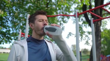 Atletik adam spor salonundaki spor şişesinden su içiyor. Parkta erkek atlet eğitimi. Zindelik ve sağlık yaşam tarzı. Susuzluk, sağlıklı yaşam tarzı ve fiziksel aktivite kavramı