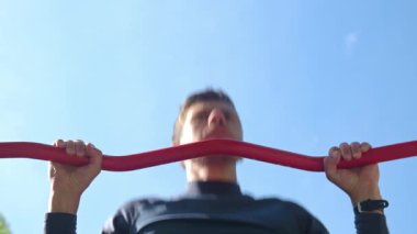 Atletik adam mavi gökyüzüne karşı kırmızı yatay çubukta barfiks çekiyor. Spor salonunda atlet eğitimi. Güç egzersizi yapan biri. Spor, spor ve sağlıklı yaşam tarzı kavramı