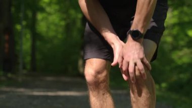 Yaz parkında antrenman yaparken dizinde ağrı olan bir koşucu. Adam koşarken yaralanmış. Spor sonrası diz ağrısı çeken erkek sporcu.