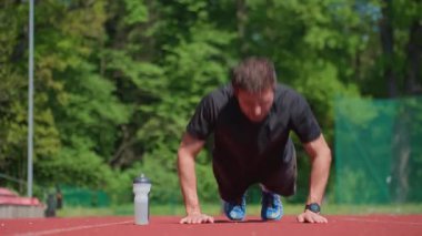 Atletik adam kırmızı pistte barfiks çekiyor. Yanında da su şişesi var. Açık hava antrenmanı. Stadyumda insan eğitimi. Etkin yaşam tarzı, spor ve spor konsepti