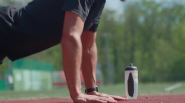Atletik adam kırmızı pistte barfiks çekiyor. Yanında da su şişesi var. Açık hava antrenmanı. Stadyumda insan eğitimi. Etkin yaşam tarzı, spor ve spor konsepti