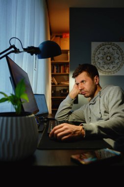 Odaklanamayan adam masada oturuyor, eli yüzü üzerinde, ekrana bakıyor. Ofiste Freelancer 'ın dikkati dağıldı. Erteleme, aşırı çalışma ve dijital yanma kavramı
