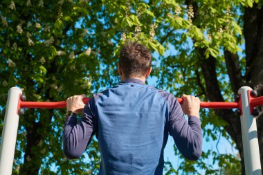 Atletik adam parktaki kırmızı yatay barda barfiks çekiyor. Spor salonunda üst vücut kaslarını çalıştıran bir sporcu. Güç egzersizi yapan biri. Spor, spor ve sağlıklı yaşam tarzı kavramı