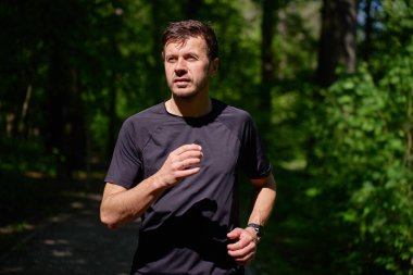 Yaz günü Yeşil Park 'ta koşan bir adam. Doğada kardiyo eğitimi. Erkek koşucu orman yolunda koşuyor. Refah ve aktif yaşam tarzı kavramı