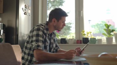 Ekose gömlekli bir adam akıllı telefon kullanırken beyaz kaseden yulaf lapası yiyor. Erkek kahvaltıda telefona bakıyor. Sosyal medya bağımlılığı, dikkat dağıtma ve dijital bağımlılık kavramı