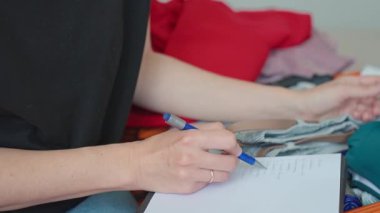 Seyahate hazırlanan bir kadın, bavulunu elbiseleriyle dolduran ve seyahat listelerini kontrol eden bir kadın. Tatil ve tatil planlama kavramı