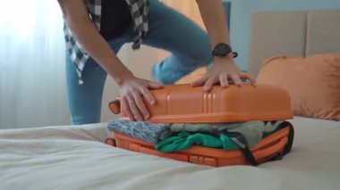 Yolculuktan önce turuncu bavulu kapatmaya çalışan bir adam. Erkek gezgin bir sürü giysi hazırlarken, seyahat için hazırlanırken zorlanır.