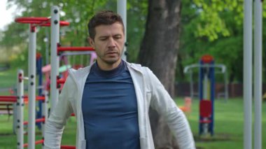 Spor giyimli bir adam yeşilliklerle çevrili açık hava spor salonunda esniyor. Atletik adam antrenmandan önce parkta ısınıyor. Zindelik, sağlıklı yaşam tarzı ve sağlık kavramı