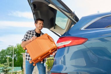 Turuncu bavulu yolculuktan önce bagaja yükleyen adam. Seyahat için bavullar