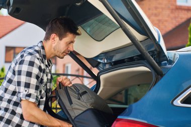 Yolculuk için bir adam sırt çantasını arabanın bagajına yüklüyor. Bagajları araca koyarak yolculuk için hazırlanıyoruz. Açık hava yolculuğu kavramı