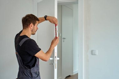 İşçi, balon seviyesiyle kapının dikey hizasını kontrol ediyor. Profesyonel iç kapı döşemesi. Ev yenilenmesi