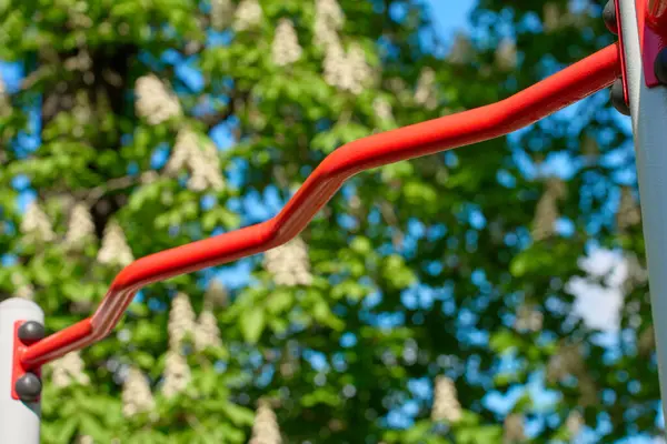 Parkta barfiks çekmek için kırmızı dalgalı maymun barı. Arka planda ağaçlar ve gökyüzü var. Spor eğitimi için açık spor aletleri. Spor anlayışı, açık hava egzersizi ve aktif yaşam tarzı