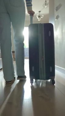 Dolaşan bavullarla kapıya doğru yürüyen gezginin alçak açılı görüntüsü. Koridorda turuncu bavulla yürüyen kişi. Ayrılma ve tatil için evden ayrılma kavramı